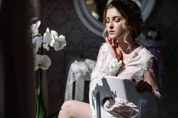 Le matin de la mariée. Mariage d'art. Portrait d'une jeune mariée en boudoir de dentelle blanche aux cheveux blonds ondulés et un bouquet à la main posant timidement vers le bas — Photo