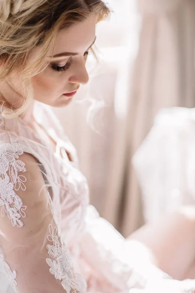 Menyasszony reggel. Képzőművészeti esküvő. Egy fiatal menyasszony fehér csipke budoár hullámos szőke hajjal és egy csokor a kezében pózol, lenézett félénken portréja — Stock Fotó