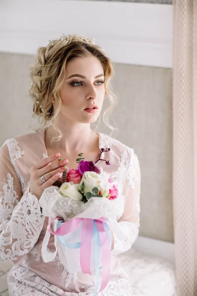 Le matin de la mariée. Mariage d'art. Portrait d'une jeune mariée en boudoir de dentelle blanche aux cheveux blonds ondulés et un bouquet à la main posant timidement vers le bas — Photo