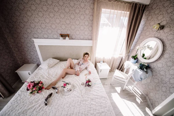 Porträt einer jungen, charmanten Blondine in weißen Dessous. auf einem großen Bett mit Kuchen und Schuhen — Stockfoto