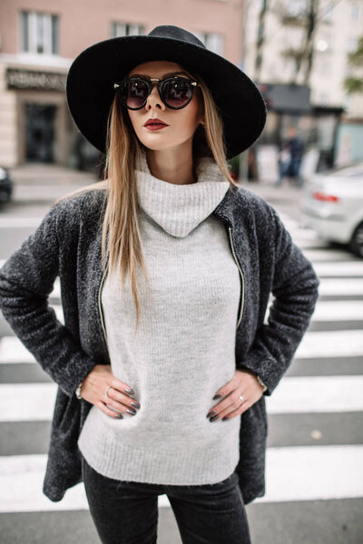 Closeup portrait of a young beautiful fashionable woman wearing sunglasses. A model in a stylish wide-brimmed hat on a pedestrian crossing