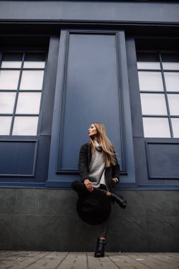 Portre portre genç bir güzel moda kadın güneş gözlüğü takıyor. Manken şapkalı şık geniş ekledi mavi bir arka plana dayanır. Gri tonları uyum benzer giysilerle. Uleach tarzı