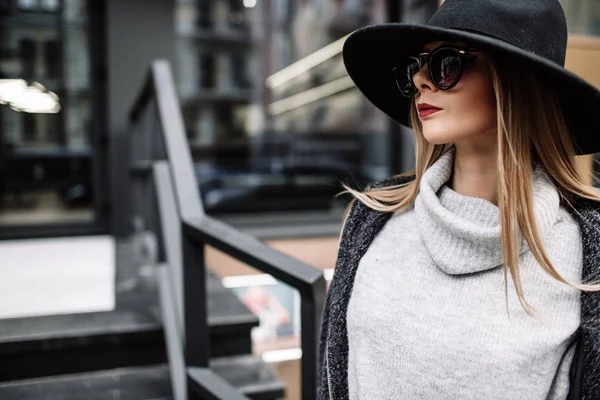 Primo piano ritratto di una giovane bella donna alla moda che indossa occhiali da sole. Un modello in un elegante cappello a tesa larga. Vestiti armoniosamente simili nei toni del grigio. Uleach stile di tiro. Moda donna — Foto Stock