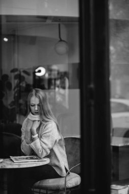 Kız bir kafede bir masada kahve, içecekler çay, görünüm pencere camı delip, moda vurdu