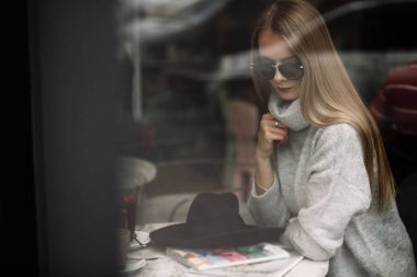 Kız bir kafede bir masada kahve, içecekler çay, görünüm pencere camı delip, moda vurdu