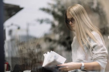 Kız bir kafede bir masada kahve, içecekler çay, görünüm pencere camı delip, moda vurdu