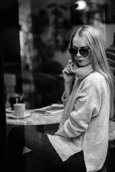 Kız bir kafede bir masada kahve, içecekler çay, görünüm pencere camı delip, moda vurdu