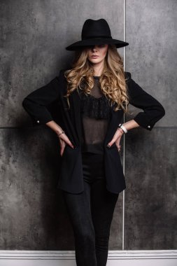 Güzel genç gizemli sarışın kız siyah şapka ve gri arka plan üzerinde siyah ceket. Gözleri bir şapka ile kaplıdır. Manikür - uzun kırmızı tırnaklar, tırnak cilası. Moda, güzellik.