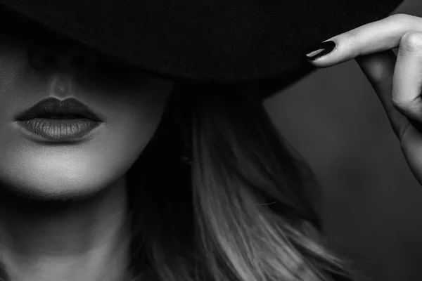 Beautiful young mysterious blond girl in black hat and black jacket on gray background. Eyes are covered with a hat. Manicure - long red nails, nail polish. Fashion, beauty. — Stock Photo, Image