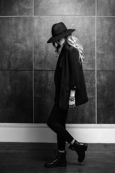 Beautiful young mysterious blond girl in black hat and black jacket on gray background. Eyes are covered with a hat. Manicure - long red nails, nail polish. Fashion, beauty. — Stock Photo, Image