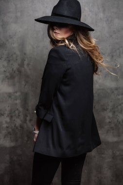 Güzel genç gizemli sarışın kız siyah şapka ve gri arka plan üzerinde siyah ceket. Gözleri bir şapka ile kaplıdır. Manikür - uzun kırmızı tırnaklar, tırnak cilası. Moda, güzellik.