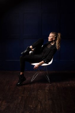 Seksi genç model beyaz sandalye p üzerinde oturmuş, bir karanlık giysili