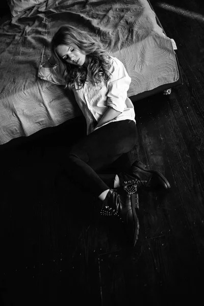 Una ragazza con lunghi capelli biondi vestita in jeans neri, una camicia a righe e scarpe nere seduta sul letto con biancheria blu. Abito casual alla moda . — Foto Stock