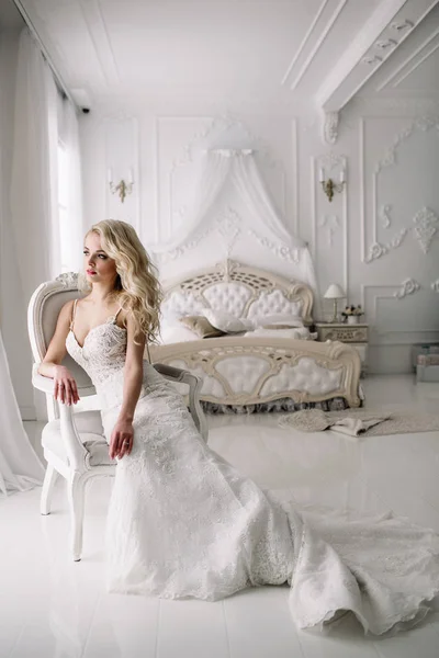 Wedding. Bride in a beautiful dress indoors in a white studio, like at home. The fashionable wedding style is taken in full length. Young attractive blond model with curly hair, like a bride