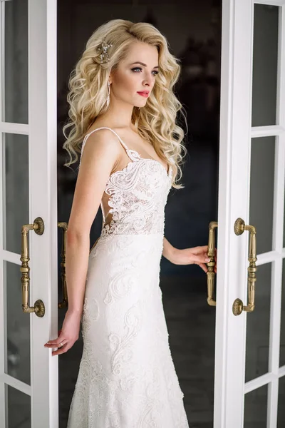 Wedding. Bride in a beautiful dress indoors in a white studio, like at home. The fashionable wedding style is taken in full length. Young attractive blond model with curly hair, like a bride