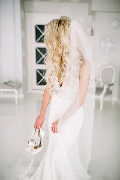 Wedding. Bride in a beautiful dress indoors in a white studio, like at home. The fashionable wedding style is taken in full length. Young attractive blond model with curly hair, like a bride