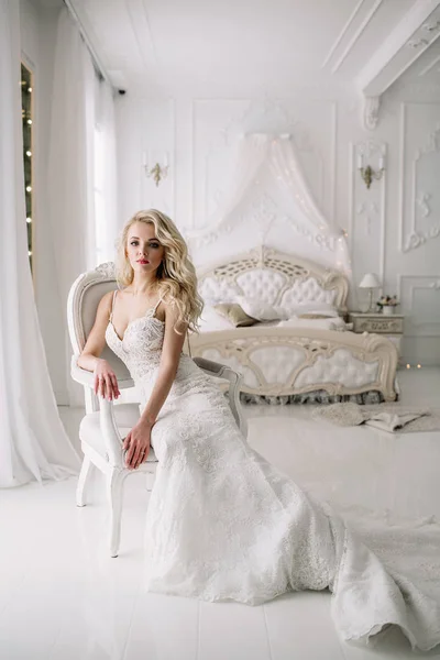 Casamento. Noiva em um lindo vestido dentro de casa em um estúdio branco, como em casa. O estilo de casamento na moda toma-se no comprimento cheio. Jovem modelo loiro atraente com cabelo encaracolado, como uma noiva — Fotografia de Stock