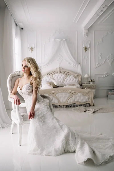 Свадьба. Невеста в красивом платье в помещении в белой студии, как дома. Модный свадебный стиль берется в полную длину. Молодая привлекательная блондинка с вьющимися волосами, как невеста — стоковое фото