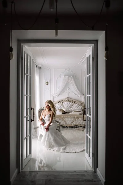 Свадьба. Невеста в красивом платье в помещении в белой студии, как дома. Модный свадебный стиль берется в полную длину. Молодая привлекательная блондинка с вьющимися волосами, как невеста — стоковое фото
