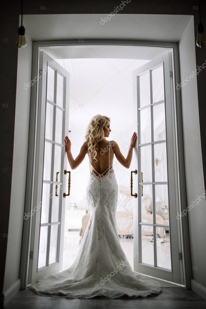 Wedding. Bride in a beautiful dress indoors in a white studio, like at home. The fashionable wedding style is taken in full length. Young attractive blond model with curly hair, like a bride