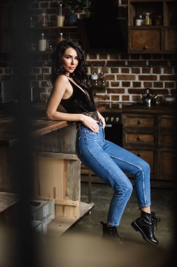 Güzel esmer kahverengi ahşap mobilya, mutfak, modern ev hanımı, moda mavi kot pantolon ve mavi bir gömlek giymiş