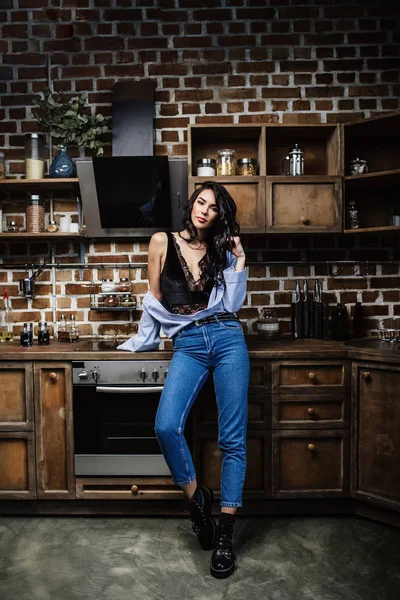 Vacker brunett i kök, modern hemmafru, mode, bruna trämöbler, klädd i blå jeans och en blå skjorta — Stockfoto