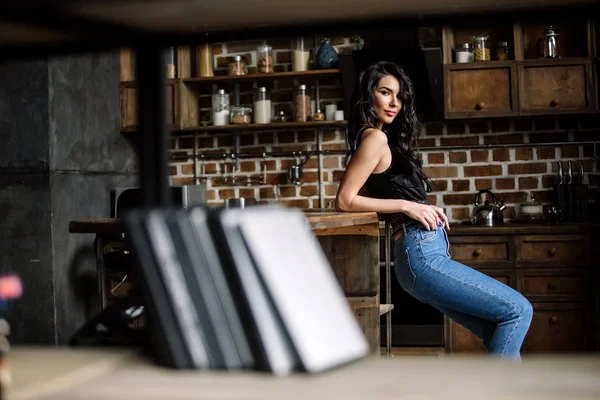 Linda morena na cozinha, dona de casa moderna, moda, móveis castanhos de madeira, vestidos com jeans azul e uma camisa azul — Fotografia de Stock