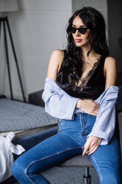 güneş gözlüğü, mavi tişört, mavi kot pantolon ve iç oda güzel bir esmer portresi