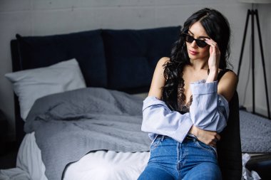 güneş gözlüğü, mavi tişört, mavi kot pantolon ve iç oda güzel bir esmer portresi