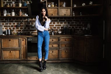 Güzel esmer kahverengi ahşap mobilya, mutfak, modern ev hanımı, moda mavi kot pantolon ve mavi bir gömlek giymiş