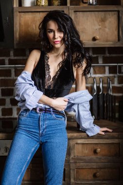 Güzel esmer kahverengi ahşap mobilya, mutfak, modern ev hanımı, moda mavi kot pantolon ve mavi bir gömlek giymiş