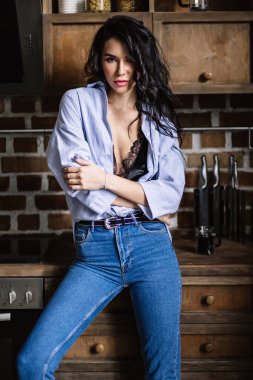 Güzel esmer kahverengi ahşap mobilya, mutfak, modern ev hanımı, moda mavi kot pantolon ve mavi bir gömlek giymiş