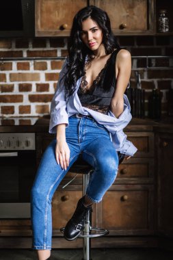 Güzel esmer kahverengi ahşap mobilya, mutfak, modern ev hanımı, moda mavi kot pantolon ve mavi bir gömlek giymiş