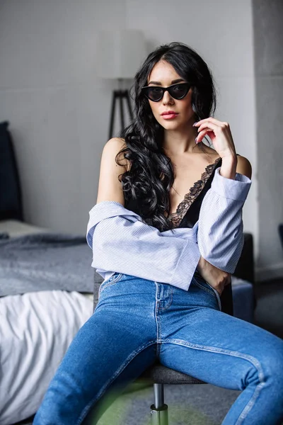 Porträt einer schönen Brünette mit Sonnenbrille, blauem Hemd, blauer Jeans und Interieur im Zimmer — Stockfoto