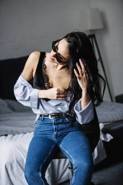 Portrait d'une belle brune en lunettes de soleil, chemise bleue, jeans bleus et intérieur dans la chambre — Photo