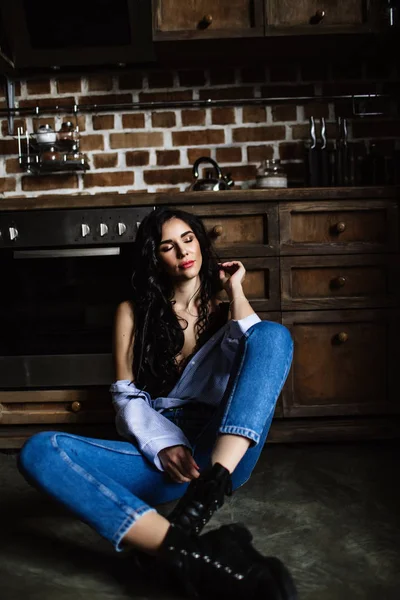 Linda morena na cozinha, dona de casa moderna, moda, móveis castanhos de madeira, vestidos com jeans azul e uma camisa azul — Fotografia de Stock