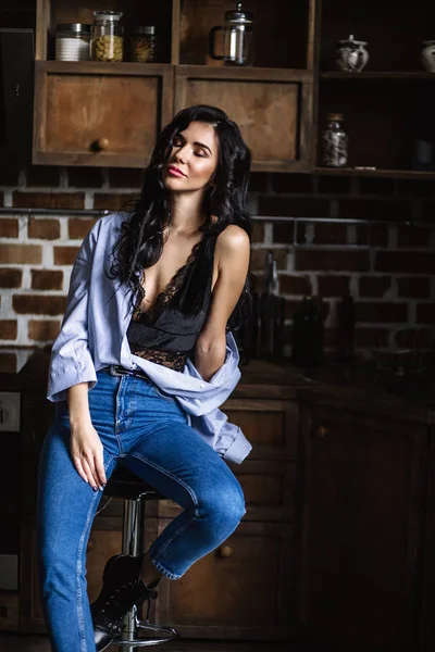 Linda morena na cozinha, dona de casa moderna, moda, móveis castanhos de madeira, vestidos com jeans azul e uma camisa azul — Fotografia de Stock