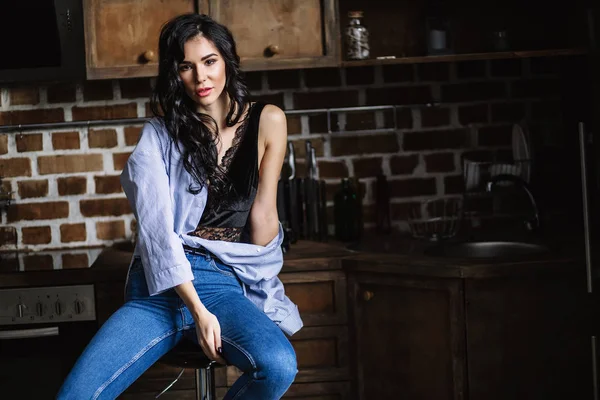 Hermosa morena en la cocina, ama de casa moderna, moda, muebles marrones de madera, vestidos con vaqueros azules y una camisa azul — Foto de Stock