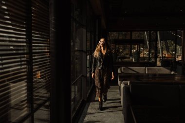 Güzel bir çatı katının içindeki bir restoranda güzel bir manken kız. Güneş gözlüğü takıyor, deri ceket giyiyor, günlük kıyafetler giyiyor. Sıcak fotoğrafçılık, güneş ışığı