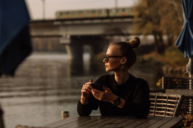 Çalışan genç bir iş kadını. Telefonda çalışıyor, telefonu elinde tutuyor, bir yatın arka planına karşı, su..