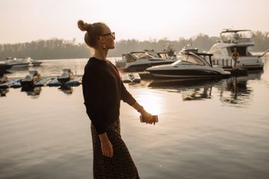 Çalışan genç bir iş kadını. Telefonda çalışıyor, telefonu elinde tutuyor, bir yatın arka planına karşı, su..