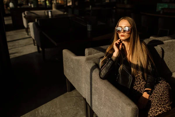 美しいロフトのインテリアのレストランで美しい女の子のモデル。サングラスの目には革の黒いジャケットを着てカジュアルな服を着ていました暖かい写真日光 — ストック写真