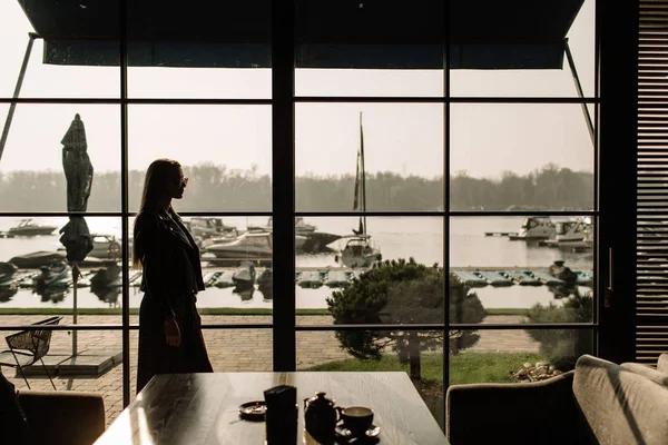 Silhouette eines jungen, stylischen Mädchens mit Sonnenbrille, das an einem Panoramafenster entlanggeht. auf dem Hintergrund der Jacht. Geschäftsfrau — Stockfoto