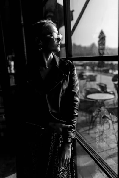 Modelo menina bonita em um restaurante em um belo interior loft. nos olhos de óculos de sol, vestido com uma jaqueta preta de couro, roupas casuais. fotografia quente, luz solar — Fotografia de Stock