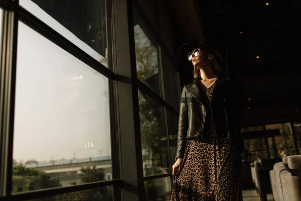 Hermosa mujer en un sombrero negro con labios rojos en gafas de sol. en medio de una ventana panorámica. mujer de negocios — Foto de Stock