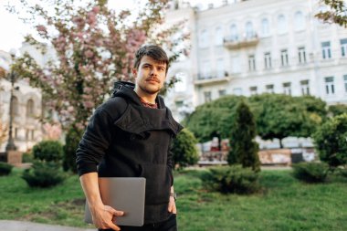 Başarılı Asyalı iş adamı elinde dizüstü bilgisayarla sokakta yürüyor.