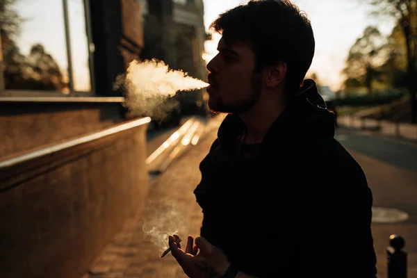 若い男は街の真ん中で日没時にタバコを吸う — ストック写真