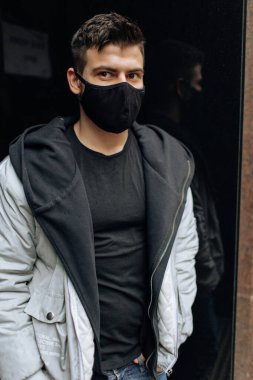 Siyah eşofmanlı esmer adam maske takıyor. Salgın bir virüs tacında siyah stil bir yüz maskesi. Virüs ve bakterilere karşı korunmak için el yapımı pamuk yüz maskesi.