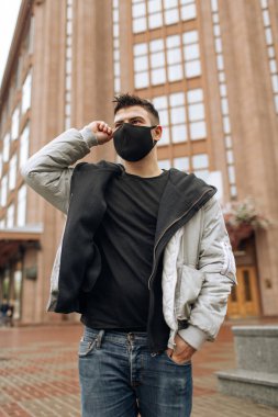 Siyah eşofmanlı esmer adam maske takıyor. Salgın bir virüs tacında siyah stil bir yüz maskesi. Virüs ve bakterilere karşı korunmak için el yapımı pamuk yüz maskesi.