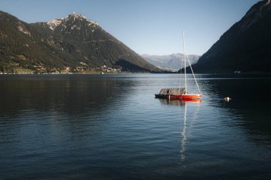 Achensee Gölü 'ndeki bir şamandıraya bağlı kırmızı tekne Avusturya Alpleri' ndeki dağlarla çevrili..